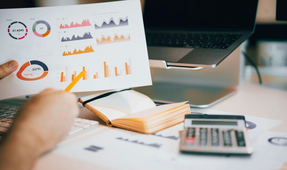 Close-up of a person analyzing financial charts and graphs with a calculator and laptop on the desk.