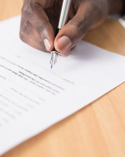 Hand signing a commercial contract with a silver pen on a wooden desk